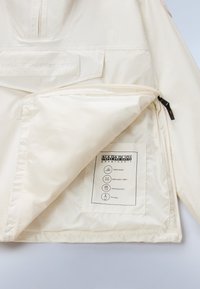 Λευκό μπουφάν με εμπρόσθιο φερμουάρ μέχρι τη μέση, διαθέτει λογότυπο, εσωτερική τσέπη και ετικέτες που υποδεικνύουν ραφές με ταινία, διαπνέον ύφασμα και αντοχή στο νερό.