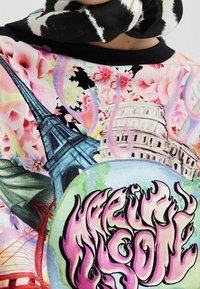 Sweat-shirt coloré avec des imprimés graphiques de monuments emblématiques, des motifs floraux et un texte en gras rose, le tout sur un fond clair.