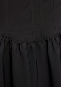 Robe noire avec un corsage ajusté comportant des coutures verticales et une jupe évasée plissée. Tissu lisse à finition mate.