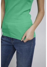 Grøn ribbet tanktop med en tætsiddende design, parret med m�ørkeblå denim jeans. Stofmaterialet er glat med en subtil tekstur.