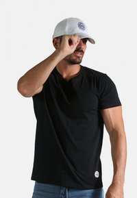 T-shirt en coton noir à manches courtes et col en V, accompagné d'une casquette de baseball blanche avec un logo circulaire.