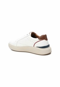 Zapatillas blancas con un cuerpo de cuero suave, detalles en cuero marrón en el talón y una suela beige. Presenta sutilezas de perforaciones en los laterales.