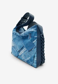 Torba w deseń dżinsowy z niebieskimi skórzanymi akcentami, z plecionym detalem po boku i z wyraźnym kształtem. Regulowany pasek z otworami.