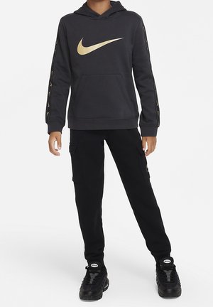 Mørkegrå hættetrøje med guld Nike-logo, kængurulomme og gulddetaljer på ærmerne. Kombineret med sorte cargobukser og sorte sneakers.