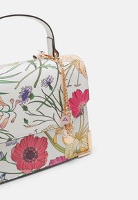Bolso floral con una superficie blanca texturizada, detalles dorados y una cadena. Presenta patrones de flores vibrantes en rosa, púrpura y amarillo.