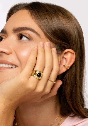 Anello in oro con pietra nera, un delicato anello a catena in oro e diversi piccoli orecchini a cerchio in oro, su uno sfondo chiaro.