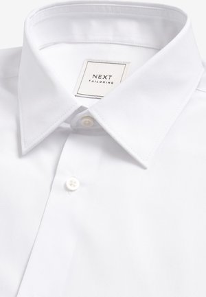 Camicia bianca con bottoni, realizzata in tessuto liscio, caratterizzata da un colletto classico, una chiusura con un solo bottone e un'etichetta con la scritta "NEXT TAILORING".