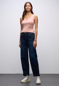 Jasnoróżowy top na ramiączkach w kształcie litery V zestawiony z ciemnoniebieskimi, luźnymi dżinsami i białymi trampkami. Prosty design z minimalnymi detalami.