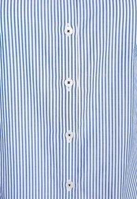 Camisa a rayas azules claras y blancas con cierre de botones frontales y seis botones blancos. Tela suave con un diseño clásico de corte recto.