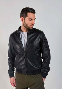 Veste bomber en cuir noir avec un col montant, fermeture éclair, poignets côtelés et une poche latérale. Finition texturée et design ajusté.