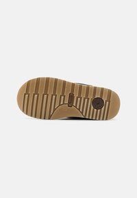 Gumi talpú sneaker, mintázott barázdával; barna kör alakú logóval és bézs színkoncepcióval rendelkezik, a tapadás és tartósság érdekében tervezve.