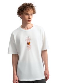 Witte katoenen T-shirt met korte mouwen, voorzien van een centrale afbeelding van een plantenpot met abstracte elementen in rode en bruine tinten.