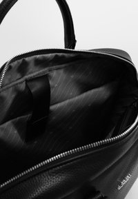 Schwarze Lederhandtasche mit strukturiertem Äußeren, silberner Reißverschlussöffnung und einem gefütterten Innenraum aus gemustertem schwarzem Stoff mit einer Tasche und einem Riemen.