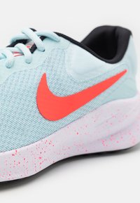 Baskets de course bleu clair avec un dessus en maille texturée, présentant un logo Nike en rose vif, un col noir et une semelle blanche avec des éclats.