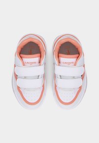 Λευκά και ροζ παιδικά αθλητικά παπούτσια Lacoste με διπλούς ιμάντες βέλκρο και επενδεδυμένους γιακάδες, απεικονιζόμενα από πάνω σε λευκό φόντο.