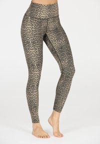 Vrouw in hoge taille, full-length leggings met luipaardprint, staand op blote voeten tegen een effen witte achtergrond.