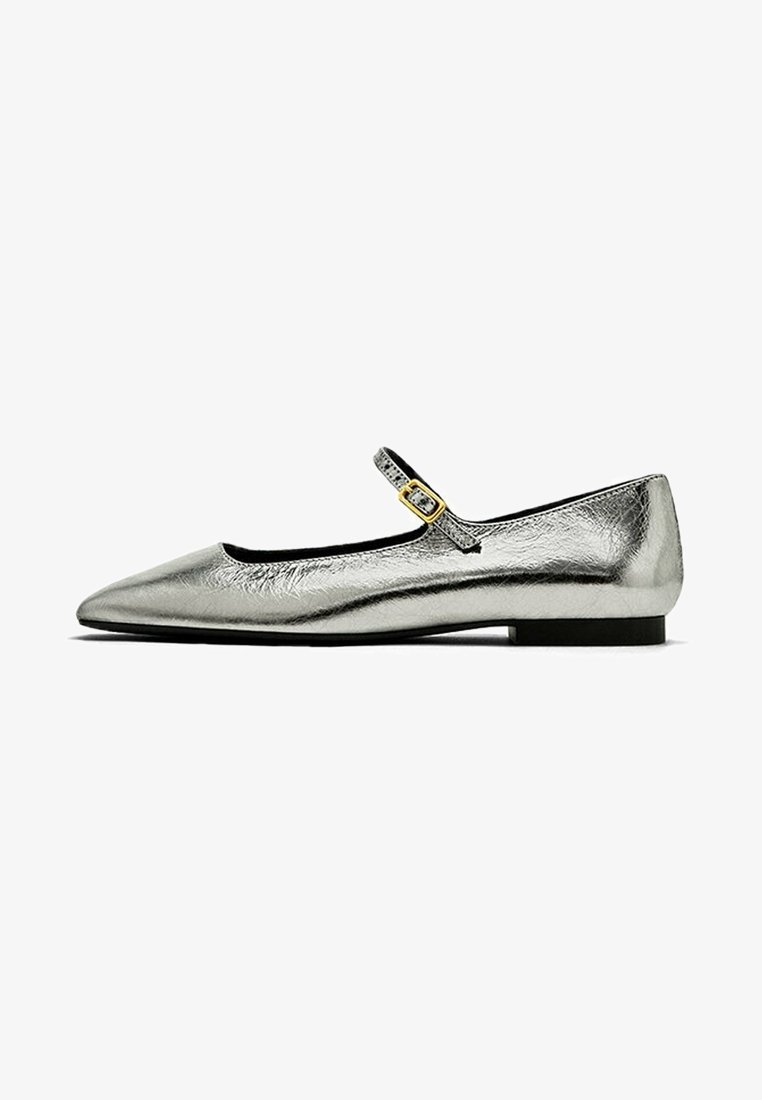 Chaussure plate Mary Jane argentée métallique pointue avec une fine bride et une petite boucle dorée sur fond blanc.