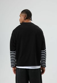 Zwart langermig shirt met wit gestreepte mouwen, gemaakt van katoen. Heeft een ontspannen pasvorm en een ronde hals.