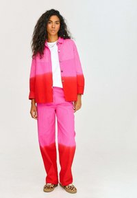 Bawełniana pikowana kurtka i dopasowane spodnie mają gradient od różowego do czerwonego. Strój zawiera białą koszulę pod spodem oraz buty w zwierzęcy wzór.