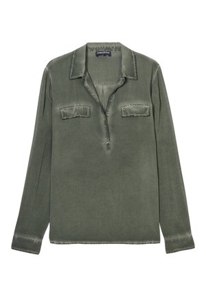 Chemise olive à manches longues en tissu doux, avec un col, deux poches sur la poitrine et une patte de boutonnage. Détails à bords bruts.