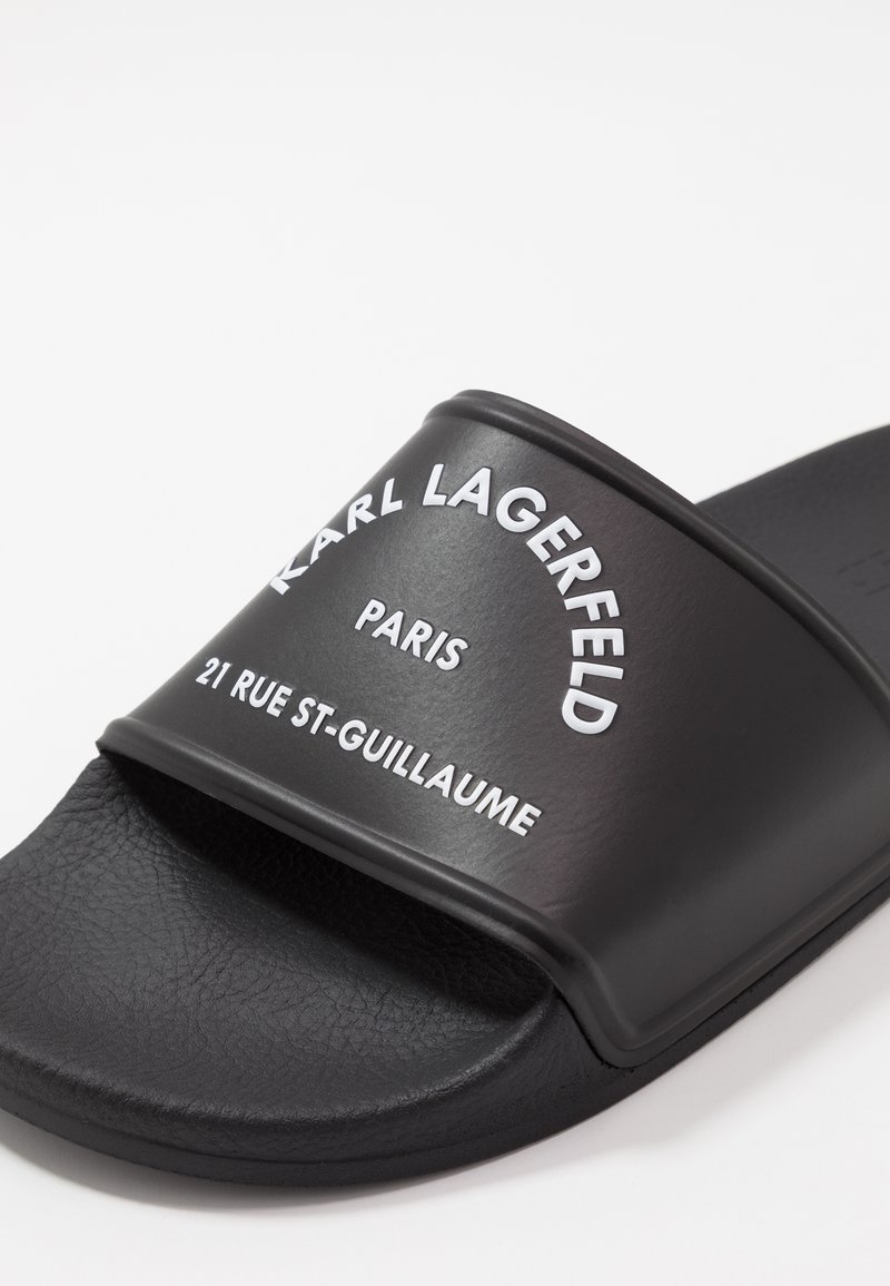 Sandale noire à enfiler avec une surface mate texturée. Présente un logo blanc bien en évidence : "KARL LAGERFELD PARIS 21 RUE ST-GUILLAUME."