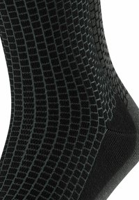 Chaussettes noires avec un motif géométrique texturé en gris foncé, dotées d'une section de orteil et de talon lisse. Le matériau semble être tricoté et extensible.