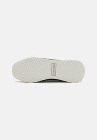 Juodas sportinių batų padas su baltu guminio dugnu, turintis žuvies kaulų raštą ir "Calvin Klein" logotipą stačiakampio akcento fone.