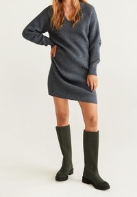 Robe pull en tricot côtelé charbon avec un col en V et des manches longues, associée à des bottes en caoutchouc vertes jusqu'aux genoux avec un talon bloc et une semelle texturée.