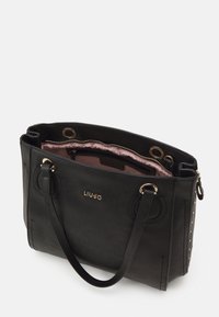 Bolso tote de cuero negro con herrajes dorados, doble asa y acentos de tachuelas. Forro de tela rosa con un bolsillo interior con cremallera.