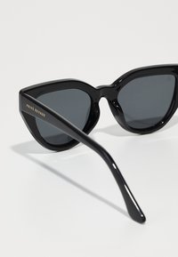 Oculos de sol pretos com formato de gato, lentes escuras, armações de plástico brilhante e marcação em dourado na haste. Apresenta pontas curvas para conforto.