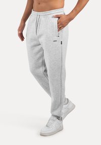 Jasnoszare spodnie dresowe wykonane z miękkiego materiału, z elastycznym paskiem w talii, bocznymi kieszeniami i dopasowanym krojem. Połączone z białymi sneakersami.