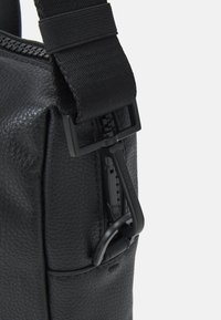 Black leather bag featuring a textured surface, a zip closure, and a sturdy adjustable strap with a black hardware accent.