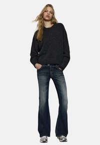 Tamnosiva široka majica s okruglim izrezom u kombinaciji s širokim plavim trapericama s osvijetljenim pranjima i srebrnim tenisicama.