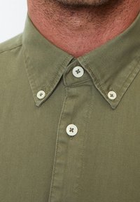 Olivově zelená košile na knoflíky s klasickým límcem, obsahující čtyři bílé knoflíky a hladkou, texturovanou tkaninu.