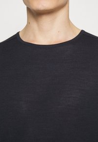 Maglietta a maniche corte a girocollo di un blu navy scuro, caratterizzata da una texture morbida e un design aderente attorno al colletto e alla zona del torace.
