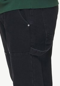 Tummansiniset farkkuhousut, joissa on rento istuvuus, sivutaskut ja näkyvät ompeleiden yksityiskohdat. Kangas on sileäpintainen ja hieman kiiltävä.