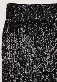 Czarna tkanina z cekinami o teksturowej powierzchni, z na przemian świecącymi czarnymi i srebrnymi okrągłymi cekinami w gęstym, wzorzystym układzie.