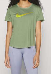 Grön sport-t-shirt med en stor gul Nike-logotyp. Har en rund halsringning, korta ärmar och en något avslappnad passform.