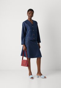 Jeansjakke med V-hals og frontlommer, parret med skjørt av denim som går til kneet. Lyseblå åpne sandaler og en liten rød håndveske.