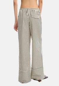 Pantaloni a gamba larga a strisce in crema e nero, con vita arricciata, tasca posteriore e orlo a contrasto. Tessuto morbido con vestibilità rilassata.