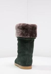 Botte en suede verte avec un épais revers en fausse fourrure grise. Bout rond et semelle en caoutchouc beige, mettant en avant des textures douces et un design de tige haute.