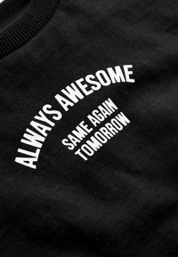 Sweatshirt en coton noir avec texte imprimé blanc : "TOUJOURS ÉTONNANT, MÊME DEMAIN." Comprend un col côtelé et une texture lisse.