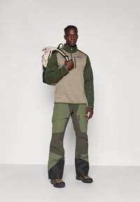 Bežo spalvos vilnonis pusiau su užtrauktuku megztinis su žaliomis rankovėmis, derinamas su žaliais ir pilkais krovininiais kelnėmis. Juodos detalės ir kišenės papildo aprangą.