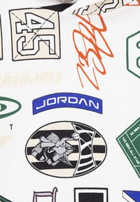 Tissu blanc arborant divers logos imprimés colorés, incluant "JORDAN" en bleu, ainsi que des graphismes liés au basketball, aux sports et aux numéros d'équipe.