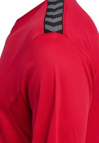 Rød sports T-shirt med en glat tekstur, der har sort og hvid stribedetaljering på skulderen. Fritstående design med rund halsudskæring.