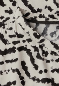 Tessuto a fantasia in bianco e nero con una morbida texture. Presenta un collo rotondo con dettagli di cucitura e una sottile lucentezza.