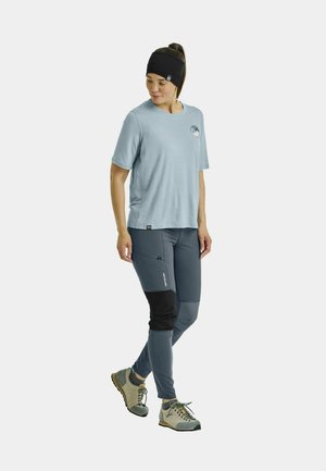 Himmelblaues Kurzarmhemd mit Logo, graue Funktionshose mit einem schwarzen Einsatz und graue Wanderschuhe mit mehrfarbigen Schnürsenkeln.