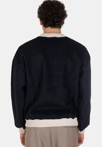 Maglione oversize blu navy con una finitura texturizzata, colletto e orlo a coste di colore crema, caratterizzato da un design semplice e una vestibilità ampia.