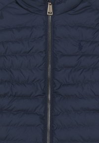 Giacca puffer blu navy con design trapuntato, chiusura a cerniera completa e dettagli del logo discreti. Realizzata in materiale leggero con una texture morbida.