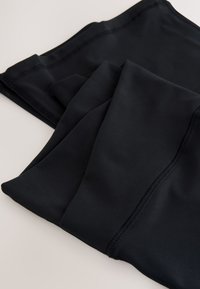 Black athletic leggings made of smooth, stretchy material, featuring flat seams and a fitted design, neatly folded in several layers.